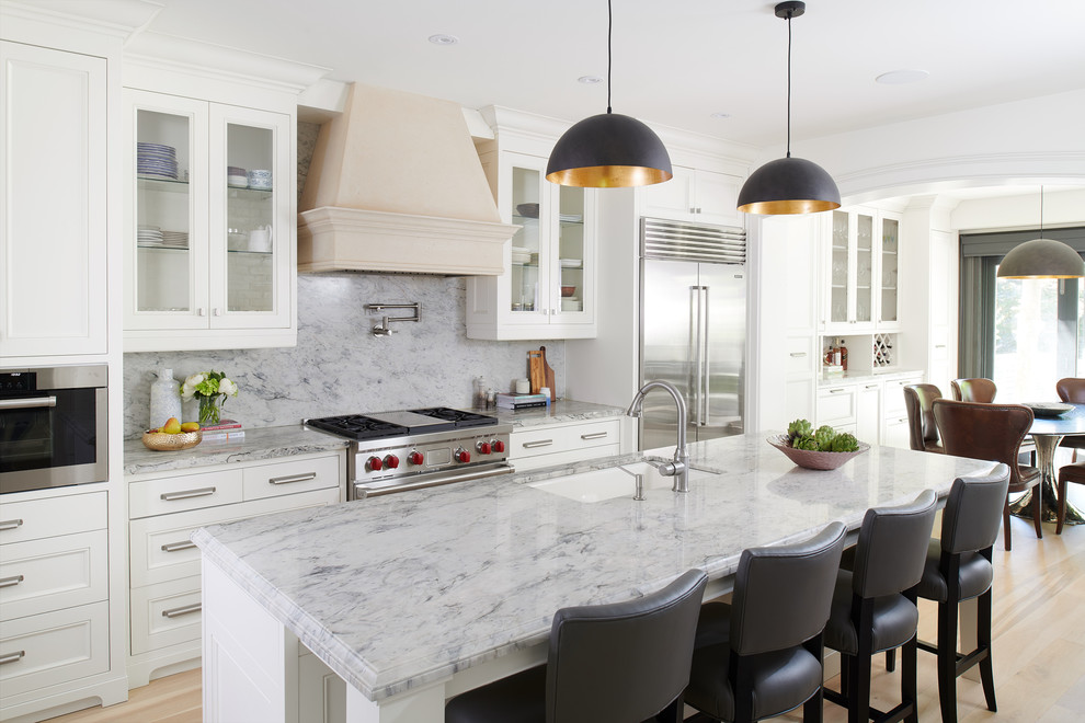 Eat-in kitchen - mid-sized traditional l-shaped beige floor and light wood floor eat-in kitchen idea in Toronto with an undermount sink, glass-front cabinets, white cabinets, gray backsplash, stone slab backsplash, stainless steel appliances, an island, gray countertops and marble countertops
