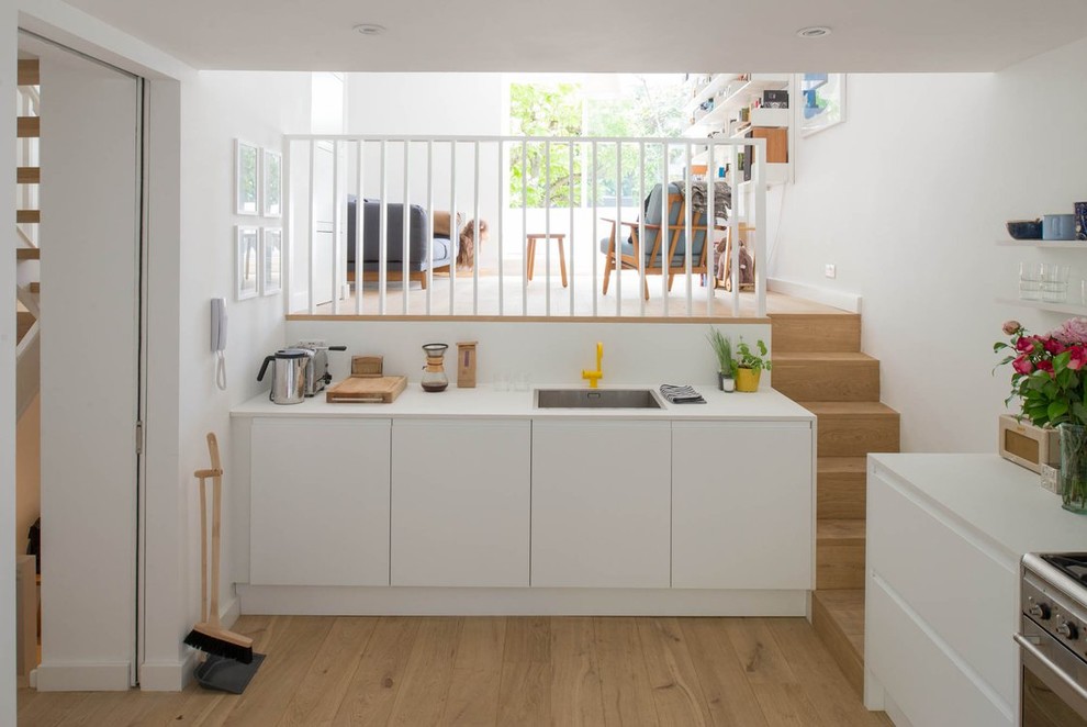 Mittelgroße Moderne Küche in L-Form mit flächenbündigen Schrankfronten, weißen Schränken und hellem Holzboden in London