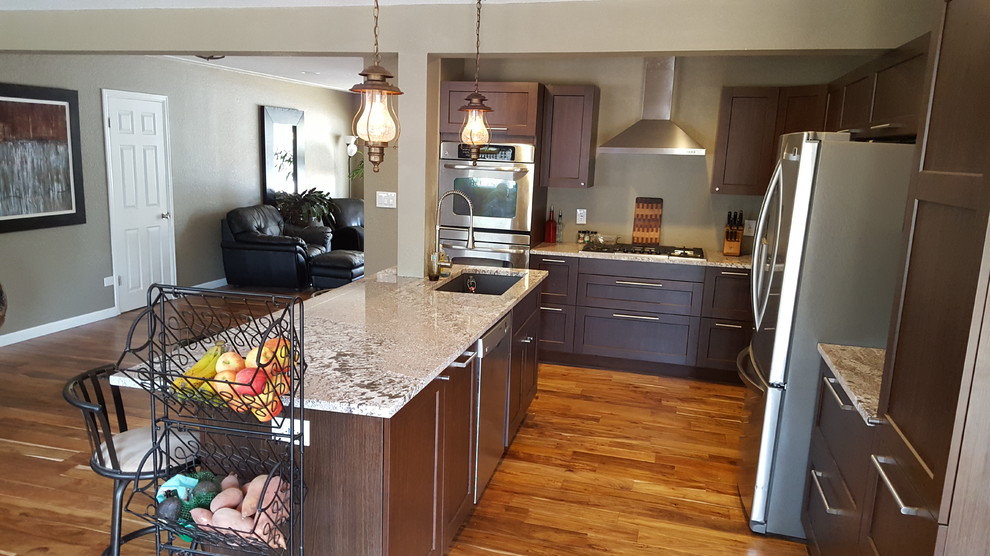 Mittelgroße Klassische Wohnküche in L-Form mit Schrankfronten im Shaker-Stil, Granit-Arbeitsplatte, Küchengeräten aus Edelstahl, Kücheninsel, Einbauwaschbecken, dunklen Holzschränken, braunem Holzboden und braunem Boden in Denver