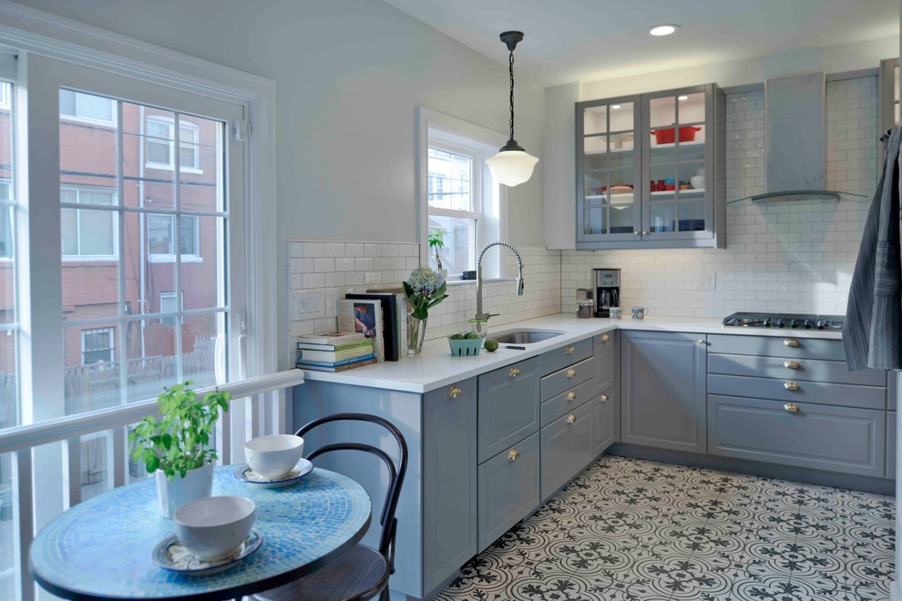 Inredning av ett klassiskt kök, med en undermonterad diskho, luckor med glaspanel, blå skåp, vitt stänkskydd, stänkskydd i tunnelbanekakel och flerfärgat golv