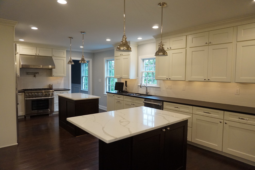 Inspiration for a large traditional l-shaped kitchen/diner in Philadelphia with a submerged sink, white splashback, metro tiled splashback, stainless steel appliances, dark hardwood flooring, multiple islands, shaker cabinets, white cabinets and engineered stone countertops.
