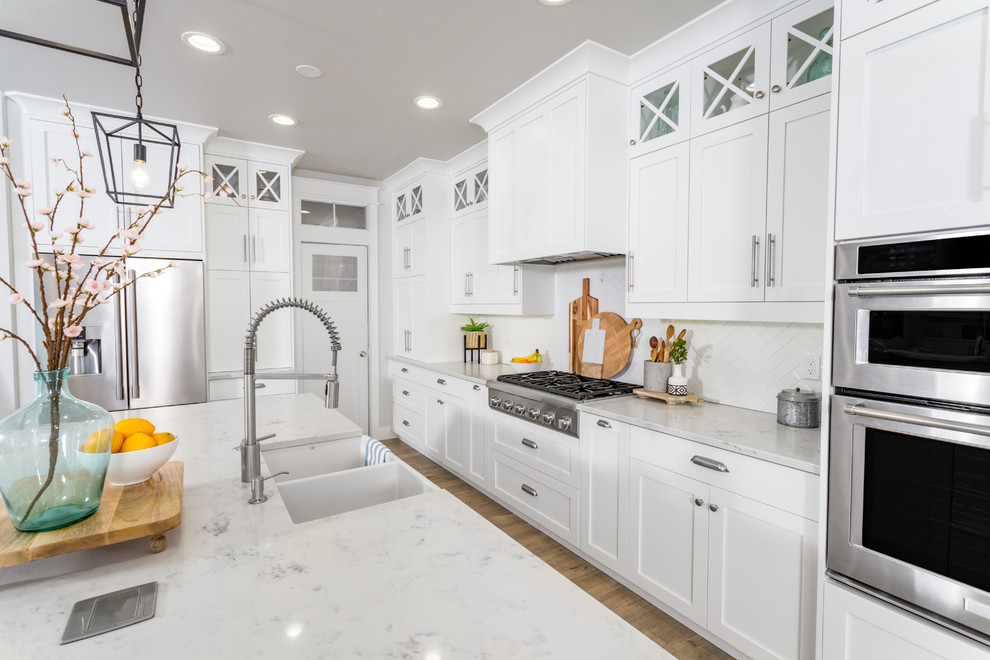 Large beach style l-shaped light wood floor and beige floor eat-in kitchen photo in San Francisco with a farmhouse sink, shaker cabinets, white cabinets, quartz countertops, white backsplash, cement tile backsplash, stainless steel appliances, an island and white countertops
