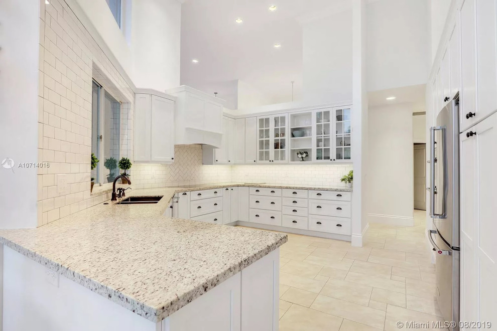 Medium sized traditional kitchen in Miami with a submerged sink, recessed-panel cabinets, white cabinets, granite worktops, white splashback, metro tiled splashback, stainless steel appliances, travertine flooring, no island, beige floors and multicoloured worktops.