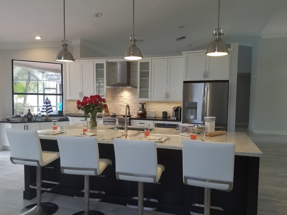 Large transitional single-wall porcelain tile and white floor open concept kitchen photo in Miami with an undermount sink, shaker cabinets, white cabinets, quartzite countertops, beige backsplash, stone tile backsplash, stainless steel appliances and an island