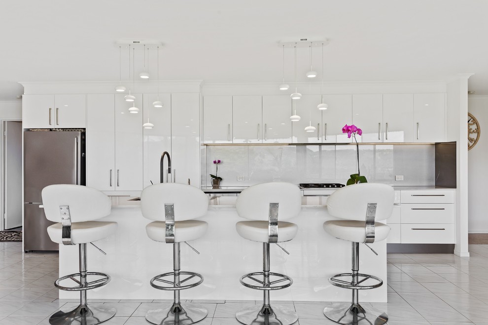 Стильный дизайн: параллельная кухня в современном стиле с обеденным столом, врезной мойкой, плоскими фасадами, белым фартуком, фартуком из стекла, техникой из нержавеющей стали, островом и белым полом - последний тренд