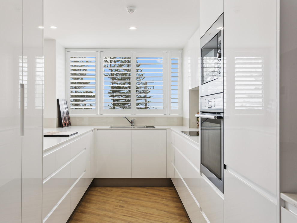 Foto på ett litet funkis vit kök, med en undermonterad diskho, släta luckor, vita skåp, bänkskiva i kvarts, beige stänkskydd, glaspanel som stänkskydd och rostfria vitvaror