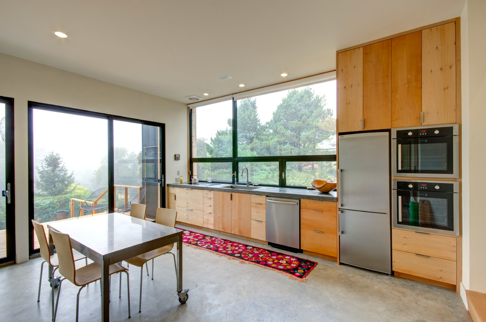 На фото: прямая кухня в современном стиле с обеденным столом, плоскими фасадами, светлыми деревянными фасадами и техникой из нержавеющей стали