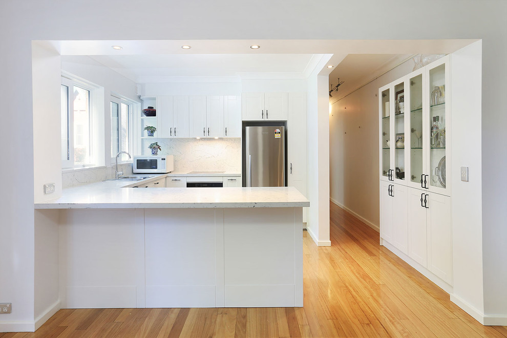 Réalisation d'une cuisine américaine tradition en U de taille moyenne avec un évier posé, un placard à porte shaker, des portes de placard blanches, un plan de travail en quartz modifié, une crédence blanche, une crédence en dalle de pierre, un électroménager en acier inoxydable, un sol en contreplaqué, un sol jaune et un plan de travail blanc.