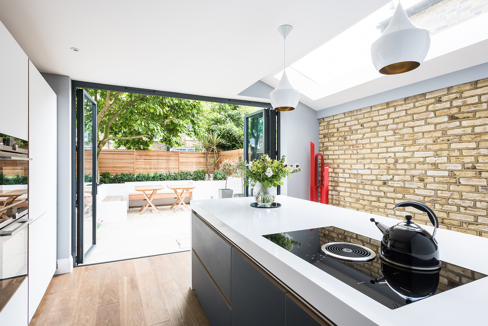 Large contemporary open plan kitchen in London with flat-panel cabinets, white cabinets, medium hardwood flooring and an island.