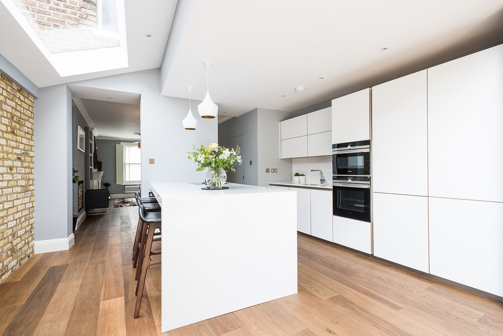This is an example of a large modern single-wall open plan kitchen in London with an integrated sink, flat-panel cabinets, white cabinets, medium hardwood flooring and an island.