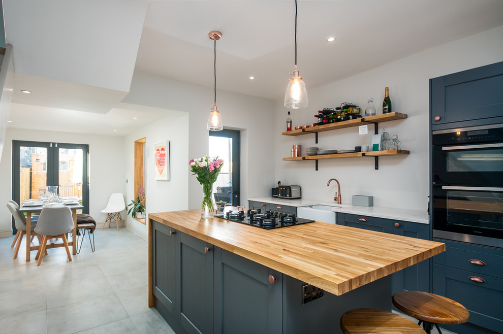 Photo of a modern galley kitchen/diner in Other with a belfast sink, shaker cabinets, blue cabinets, black appliances, an island, grey floors and white worktops.