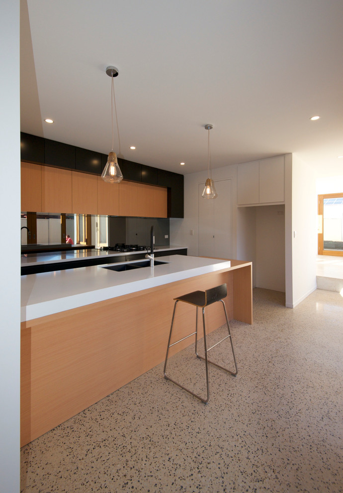 This is an example of a medium sized contemporary galley kitchen in Adelaide with a submerged sink, flat-panel cabinets, light wood cabinets, composite countertops, metallic splashback, mirror splashback, black appliances, concrete flooring and an island.