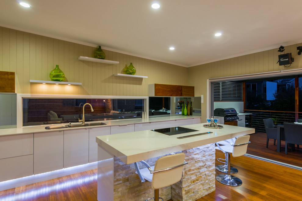 Geräumige Moderne Wohnküche mit Doppelwaschbecken, weißen Schränken, Quarzwerkstein-Arbeitsplatte, Rückwand aus Spiegelfliesen, Küchengeräten aus Edelstahl, Bambusparkett und Kücheninsel in Brisbane