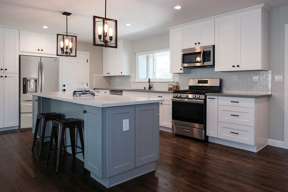 Example of a large classic l-shaped dark wood floor and brown floor eat-in kitchen design in Orange County with a drop-in sink, shaker cabinets, white cabinets, quartz countertops, white backsplash, ceramic backsplash, stainless steel appliances, an island and beige countertops