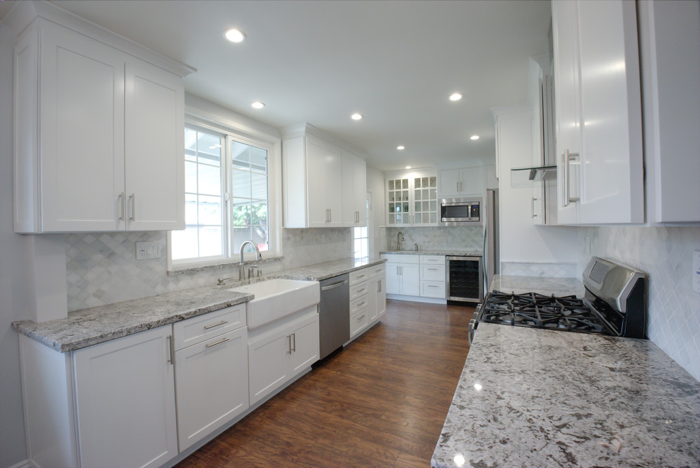 Large traditional galley kitchen/diner in Orange County with an integrated sink, shaker cabinets, white cabinets, laminate countertops, white splashback, stone tiled splashback, stainless steel appliances, medium hardwood flooring and no island.