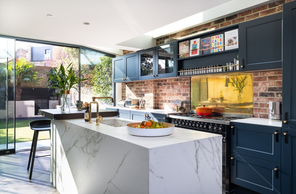 Photo of a medium sized farmhouse galley kitchen/diner in London with shaker cabinets, blue cabinets, engineered stone countertops, metallic splashback, metal splashback, black appliances, painted wood flooring, an island, white worktops and white floors.