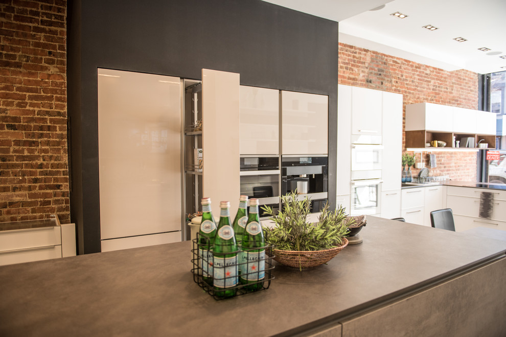 Photo of a medium sized contemporary kitchen in New York with flat-panel cabinets, white cabinets, concrete worktops, brick splashback, integrated appliances and an island.