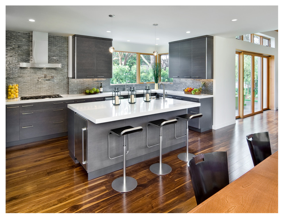 Example of a mid-sized minimalist l-shaped medium tone wood floor and brown floor eat-in kitchen design in San Francisco with a drop-in sink, flat-panel cabinets, gray cabinets, gray backsplash, stainless steel appliances and an island