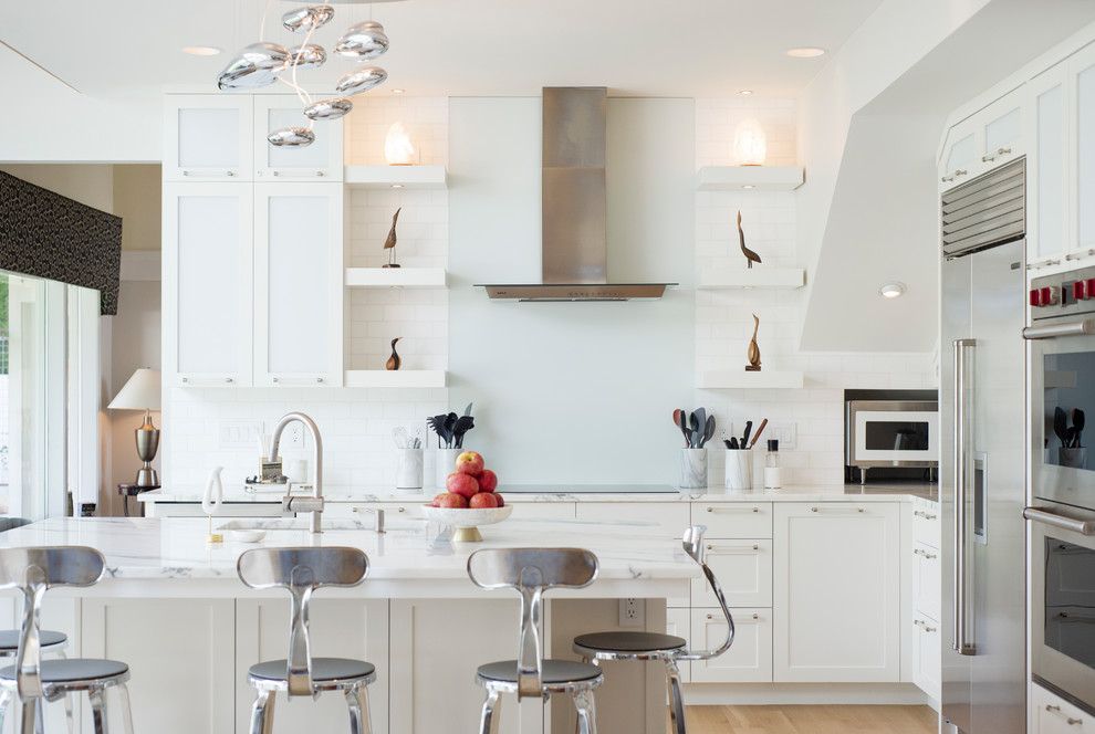 Inredning av ett modernt mellanstort vit vitt kök, med en undermonterad diskho, skåp i shakerstil, vita skåp, bänkskiva i kvartsit, vitt stänkskydd, stänkskydd i keramik, rostfria vitvaror, mellanmörkt trägolv, en köksö och brunt golv