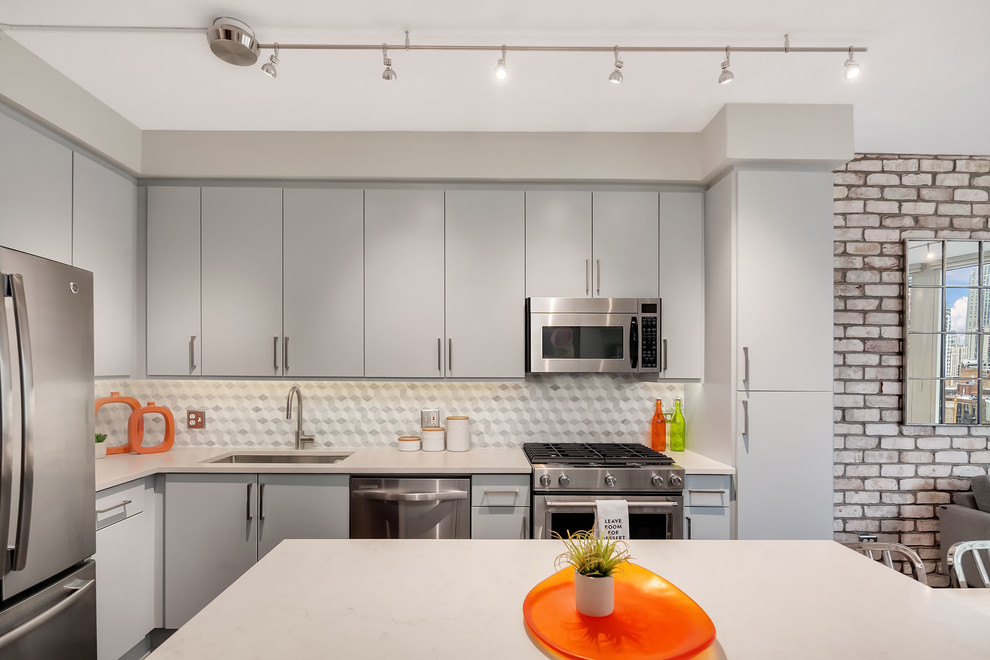 Inspiration for a small contemporary l-shaped kitchen remodel in Chicago with a single-bowl sink, flat-panel cabinets, gray cabinets, gray backsplash, stainless steel appliances and an island