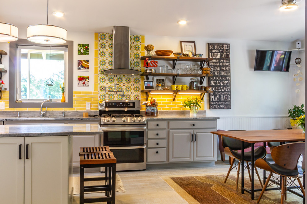 Bild på ett mellanstort eklektiskt grå linjärt grått kök med öppen planlösning, med en nedsänkt diskho, luckor med upphöjd panel, grå skåp, granitbänkskiva, gult stänkskydd, stänkskydd i porslinskakel, rostfria vitvaror, laminatgolv, en köksö och grått golv