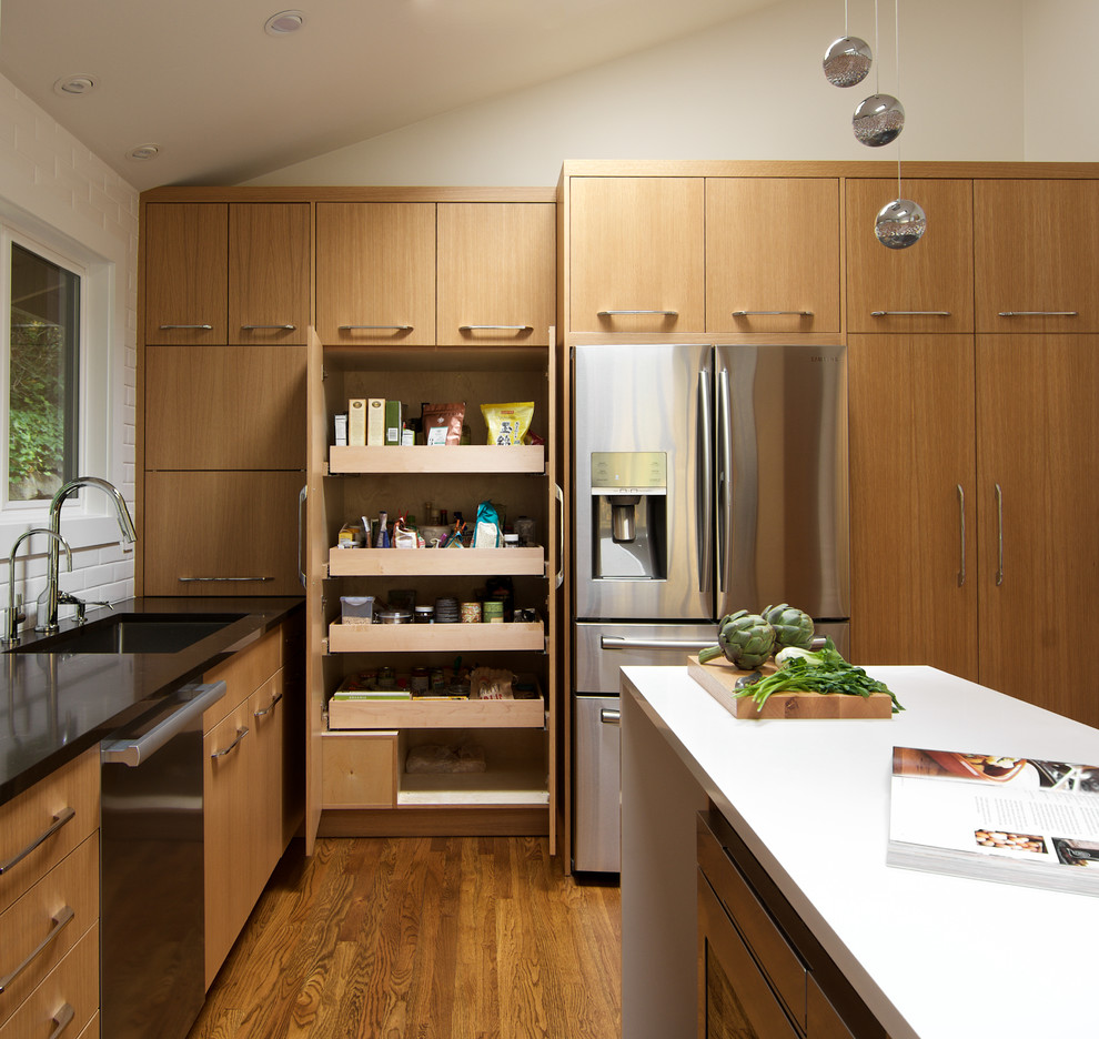 Small modern l-shaped enclosed kitchen in Seattle with a single-bowl sink, flat-panel cabinets, light wood cabinets, engineered stone countertops, white splashback, ceramic splashback, stainless steel appliances, light hardwood flooring, an island and brown floors.
