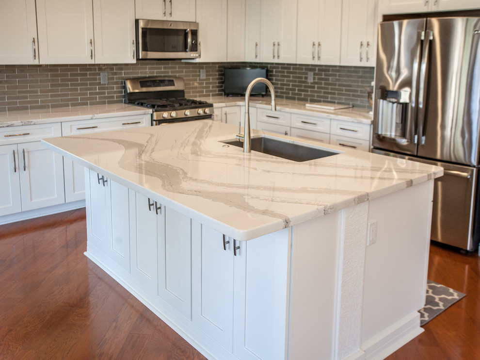 Inspiration for a transitional l-shaped eat-in kitchen remodel in Sacramento with a single-bowl sink, shaker cabinets, white cabinets, quartz countertops, gray backsplash, glass tile backsplash, stainless steel appliances and an island