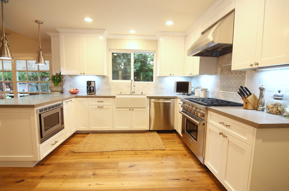 Large cottage u-shaped medium tone wood floor and brown floor eat-in kitchen photo in Los Angeles with a farmhouse sink, raised-panel cabinets, white cabinets, quartz countertops, white backsplash, porcelain backsplash, stainless steel appliances, no island and gray countertops