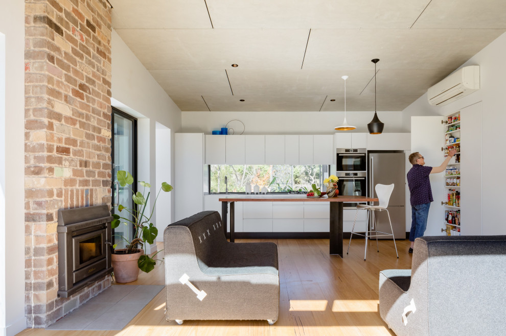Bild på ett funkis linjärt kök med öppen planlösning, med släta luckor, vita skåp, fönster som stänkskydd, rostfria vitvaror, mellanmörkt trägolv, en köksö och brunt golv