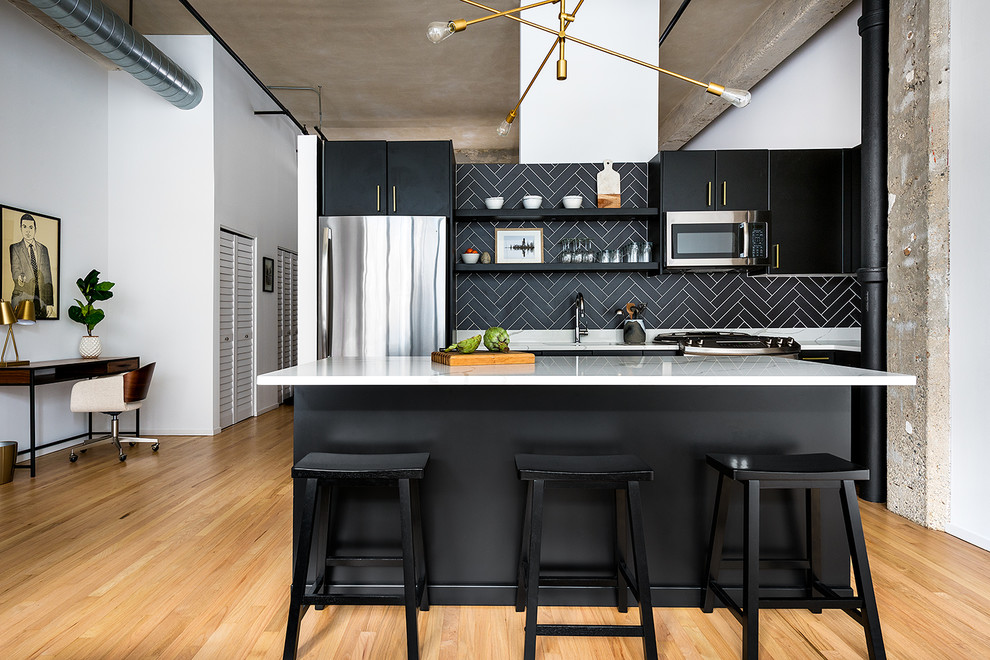 Industrial kitchen in Chicago with flat-panel cabinets, black cabinets, black splashback, stainless steel appliances, light hardwood flooring, an island and white worktops.