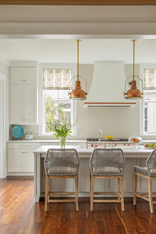 Foto på ett vit l-kök, med en rustik diskho, vita skåp, bänkskiva i kvarts, grått stänkskydd, stänkskydd i porslinskakel, integrerade vitvaror, mellanmörkt trägolv, en köksö och brunt golv
