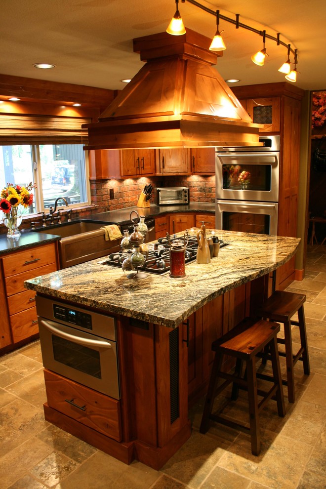 Inredning av ett klassiskt kök, med rostfria vitvaror, granitbänkskiva, en rustik diskho, skåp i mellenmörkt trä och stänkskydd i tunnelbanekakel