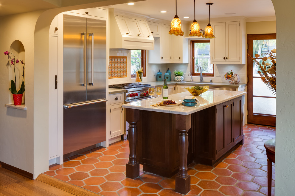 Inredning av ett amerikanskt avskilt, litet l-kök, med en undermonterad diskho, luckor med infälld panel, vita skåp, granitbänkskiva, orange stänkskydd, stänkskydd i keramik, rostfria vitvaror, klinkergolv i terrakotta och en köksö
