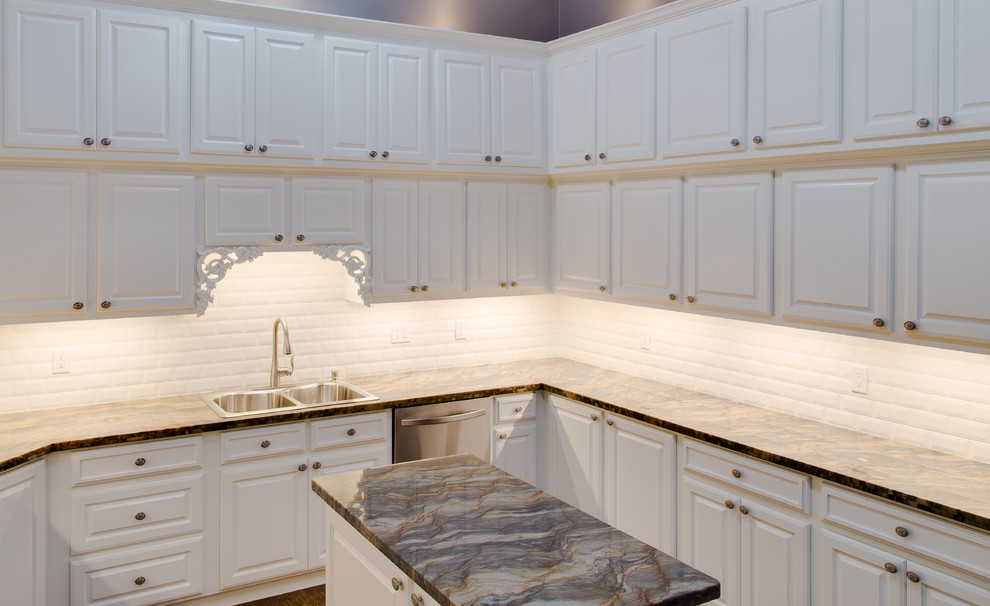 Exempel på ett klassiskt u-kök, med en nedsänkt diskho, luckor med upphöjd panel, vita skåp, bänkskiva i kvartsit, vitt stänkskydd, stänkskydd i porslinskakel, rostfria vitvaror och en köksö