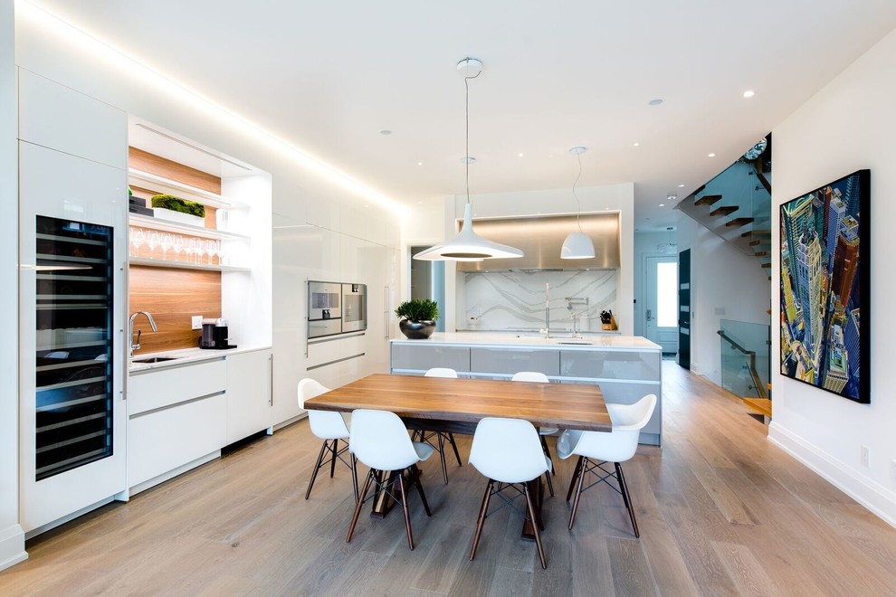 Exempel på ett mellanstort modernt kök, med en undermonterad diskho, släta luckor, vita skåp, bänkskiva i kvarts, vitt stänkskydd, rostfria vitvaror, en köksö och brunt golv