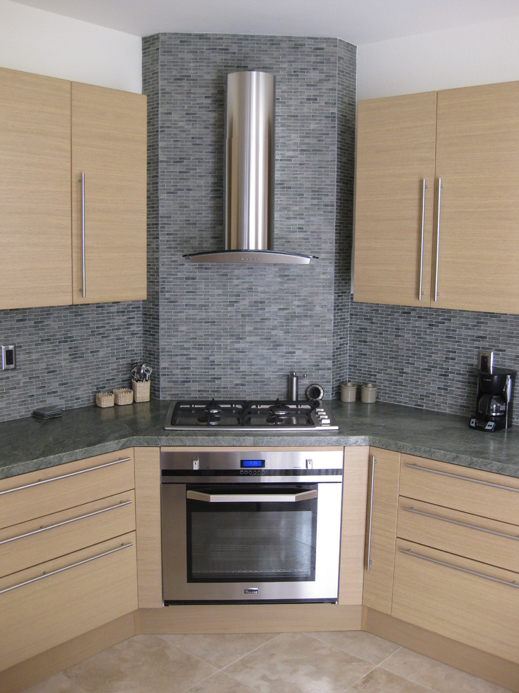 Inredning av ett modernt litet kök, med en undermonterad diskho, släta luckor, skåp i ljust trä, granitbänkskiva, grönt stänkskydd, stänkskydd i glaskakel, rostfria vitvaror och travertin golv