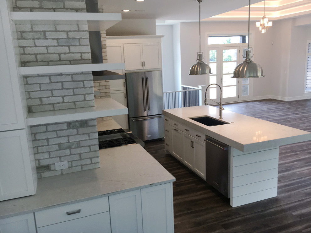 Large contemporary kitchen/diner in Other with a submerged sink, flat-panel cabinets, white cabinets, granite worktops, white splashback, brick splashback, stainless steel appliances and an island.