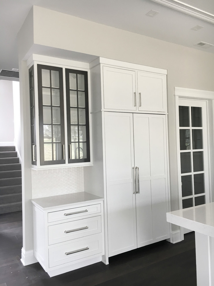 Modern inredning av ett stort kök, med en undermonterad diskho, luckor med infälld panel, vita skåp, bänkskiva i kvarts, vitt stänkskydd, stänkskydd i glaskakel, rostfria vitvaror, mörkt trägolv och en köksö