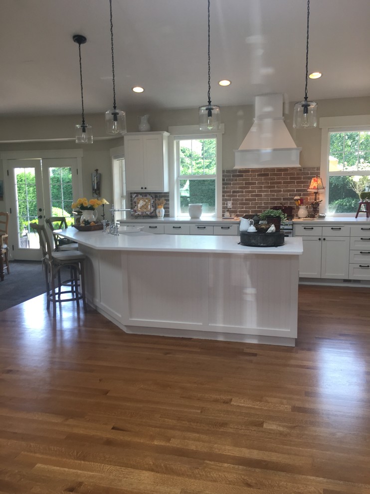 Large country light wood floor kitchen photo in Seattle with a farmhouse sink, shaker cabinets, white cabinets, quartz countertops, red backsplash, brick backsplash, stainless steel appliances, an island and white countertops
