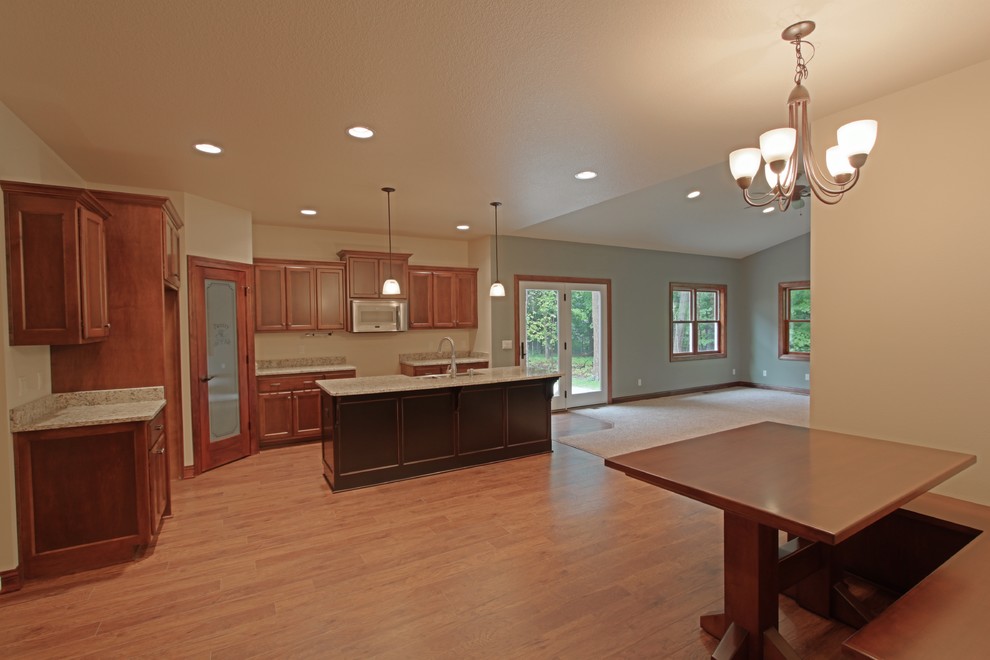 Photo of a traditional l-shaped open plan kitchen in Milwaukee with a belfast sink, shaker cabinets, dark wood cabinets, granite worktops, stainless steel appliances, medium hardwood flooring and an island.