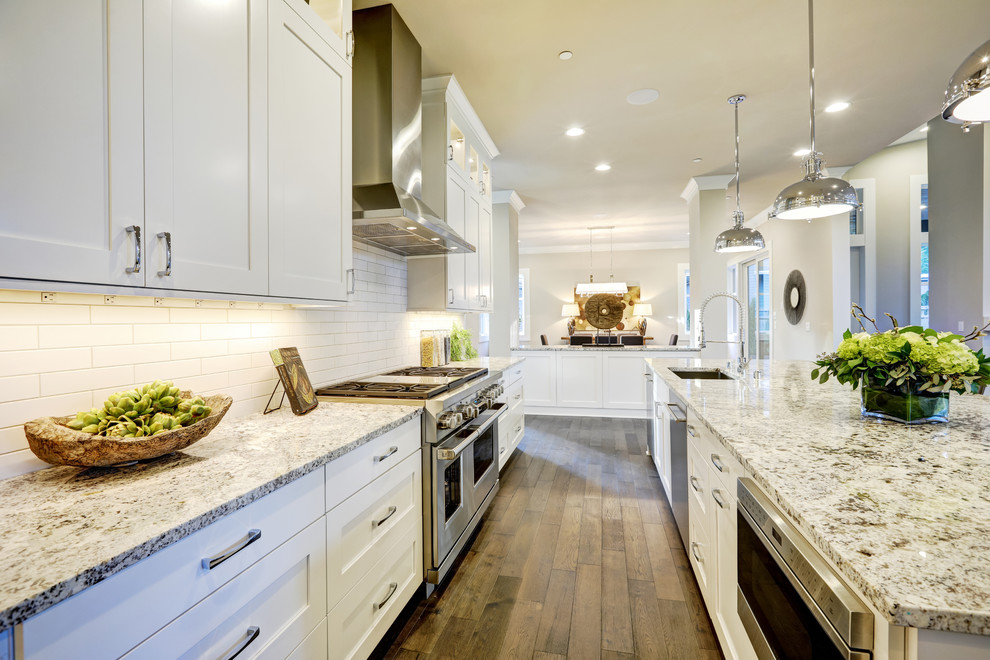 Large trendy galley medium tone wood floor and brown floor eat-in kitchen photo in Jacksonville with an undermount sink, shaker cabinets, white cabinets, quartzite countertops, beige backsplash, stainless steel appliances, an island, multicolored countertops and subway tile backsplash
