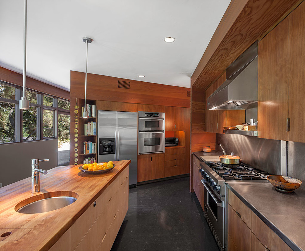 Exempel på ett modernt kök, med en köksö, en enkel diskho, släta luckor, skåp i mellenmörkt trä, stänkskydd med metallisk yta, rostfria vitvaror och bänkskiva i rostfritt stål
