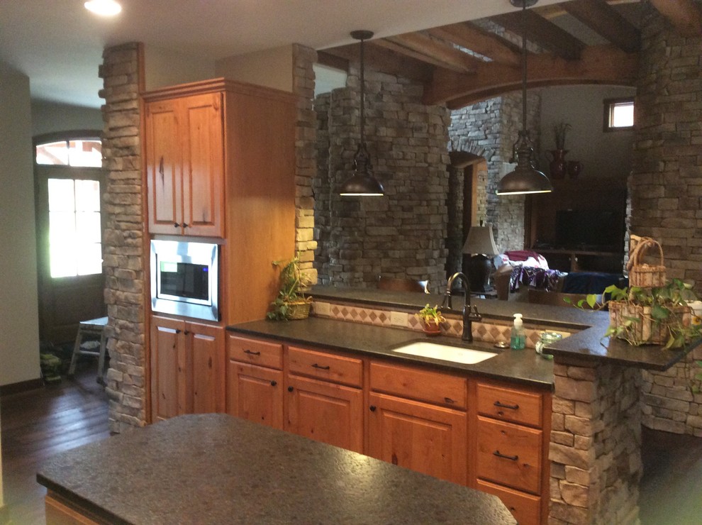 Rustik inredning av ett mellanstort kök, med en undermonterad diskho, luckor med upphöjd panel, skåp i mellenmörkt trä, svart stänkskydd, stänkskydd i keramik, rostfria vitvaror, mellanmörkt trägolv och en köksö