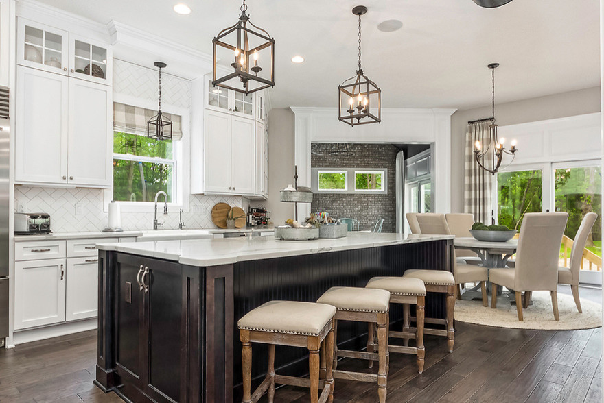 Mid-sized transitional l-shaped dark wood floor and brown floor open concept kitchen photo in Columbus with a farmhouse sink, shaker cabinets, white cabinets, marble countertops, white backsplash, porcelain backsplash, stainless steel appliances and an island