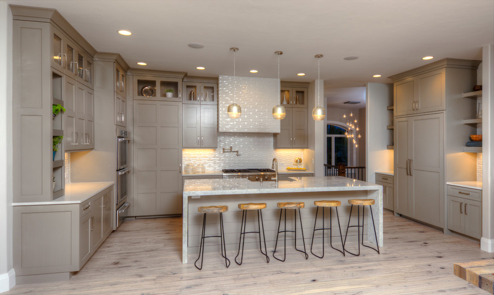 Klassische Küche mit grauen Schränken, Küchengeräten aus Edelstahl, braunem Holzboden, Kücheninsel, Schrankfronten im Shaker-Stil und Küchenrückwand in Weiß in Denver