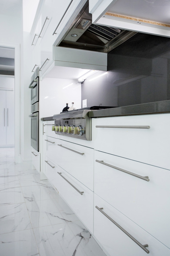 Immagine di una grande cucina moderna con lavello sottopiano, ante lisce, ante bianche, top in quarzo composito, paraspruzzi nero, paraspruzzi in lastra di pietra, elettrodomestici in acciaio inossidabile, pavimento in marmo, pavimento bianco e top bianco