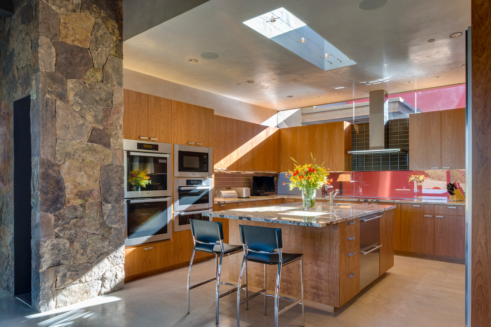 Large contemporary u-shaped kitchen in Albuquerque with flat-panel cabinets, medium wood cabinets, grey splashback, metro tiled splashback, stainless steel appliances, an island, concrete flooring, a submerged sink and soapstone worktops.