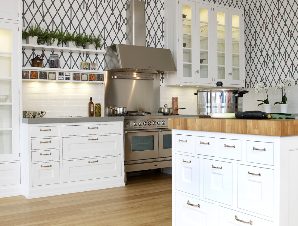 Large traditional single-wall enclosed kitchen in Stockholm with glass-front cabinets, white cabinets, white splashback, metro tiled splashback, stainless steel appliances, light hardwood flooring, an island and granite worktops.