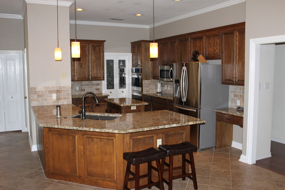 Klassische Küche mit Doppelwaschbecken, hellbraunen Holzschränken, Granit-Arbeitsplatte, Küchenrückwand in Beige, Küchengeräten aus Edelstahl und Kücheninsel in Dallas
