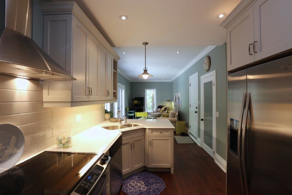 Exempel på ett avskilt, mellanstort klassiskt linjärt kök, med en dubbel diskho, skåp i shakerstil, vita skåp, bänkskiva i kvarts, vitt stänkskydd, stänkskydd i tunnelbanekakel, rostfria vitvaror, mellanmörkt trägolv, en halv köksö och brunt golv